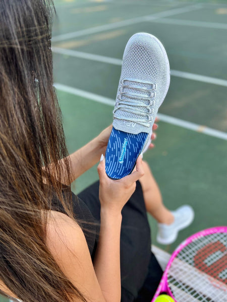 Woman placing PowerStep Pinnacle Orthotic Insole into gray tennis shoe