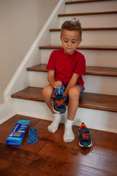 Young boy places a shoe insole for kids inside a black and orange shoe