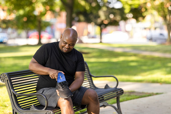 Man sitting on bench outside and placing shoe insole into black tennis shoe