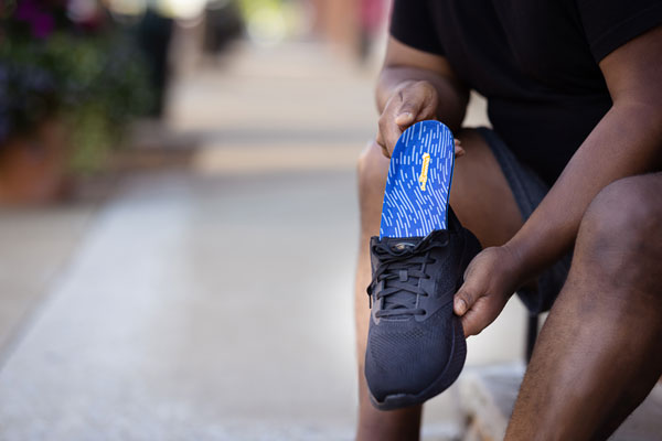 Man placing blue low arch insole for overpronation in black shoe