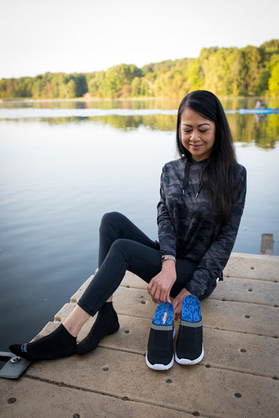 Woman sitting on dock placing blue low arch insoles into black walking shoes