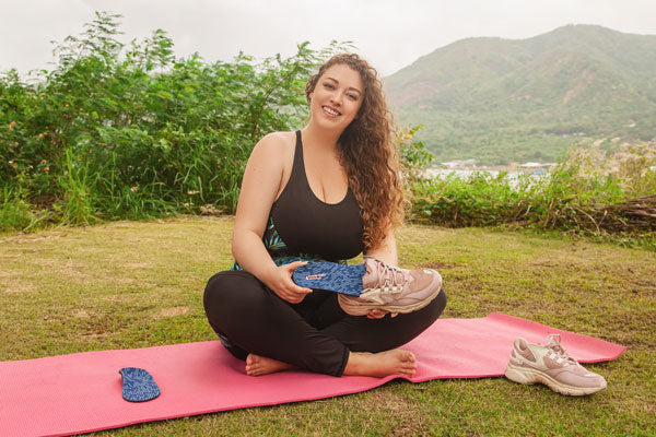 woman on yoga mat placing shoe insole into pink shoe