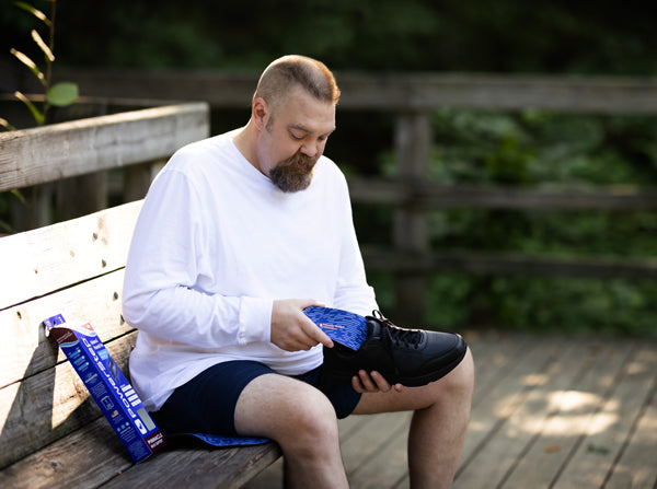 Man sitting on bench placing Pinnacle Maxx Support insole into black shoe