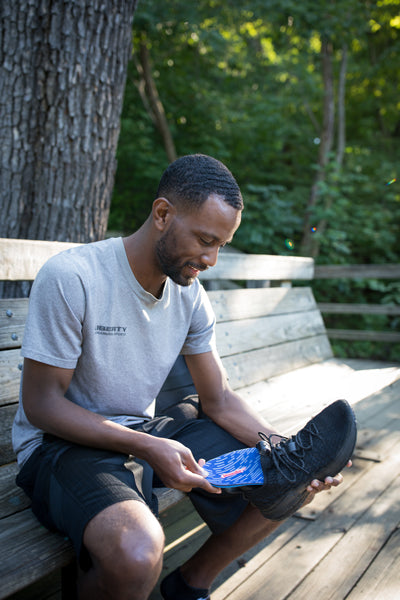 man sitting on an outdoor bench while placing a blue insole into a black shoe