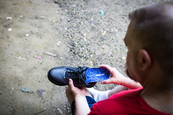 Man placing wide shoe insole into black orthopedic shoe