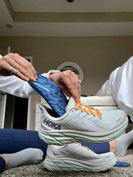 woman sitting on bedroom floor and placing arch support insole into running shoe