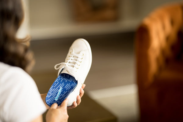 closeup of woman placing blue orthotic insole into white canvas shoe