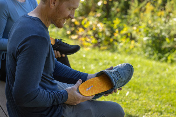 Man sitting outside placing orange running insole into gray shoe