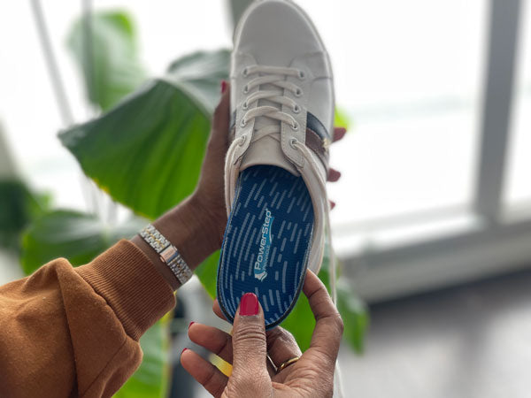 woman placing blue shoe insole into white tennis shoe