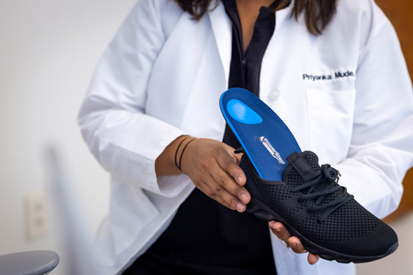 Doctor holding black tennis shoe with PowerStep ProTech orthotic inside