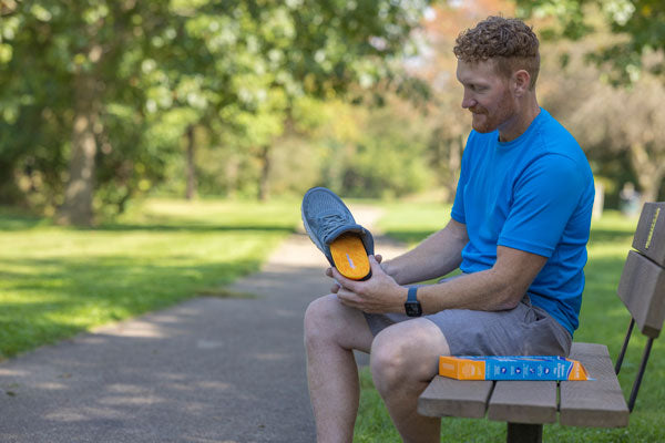 Man sitting on bench outside putting orange running insole in gray shoe