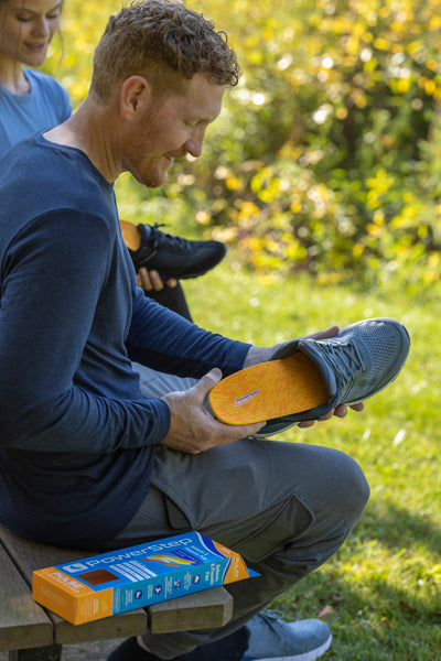 Man placing orange running shoe insole into gray tennis shoe