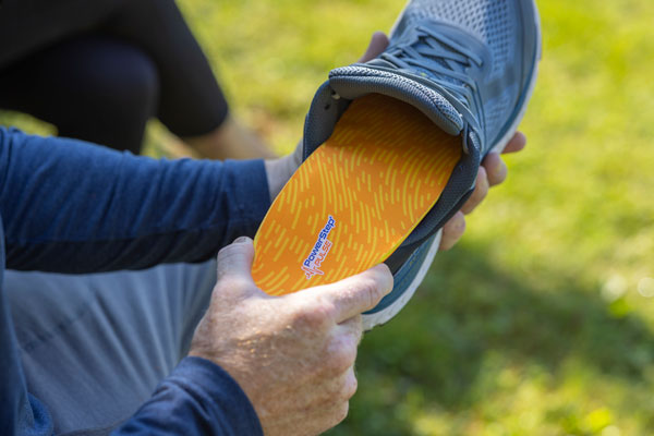 Man placing orange running shoe insole into gray tennis shoe