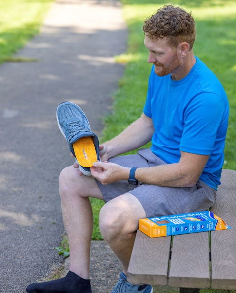 Man placing orange running shoe insole into gray shoe