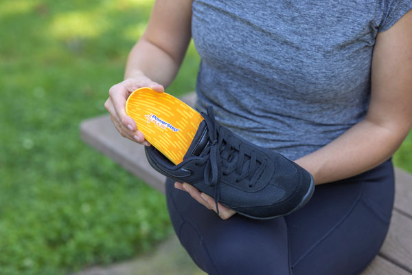 woman placing orange running shoe insole into black running shoe