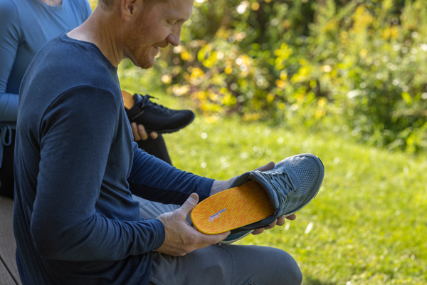 Man outside placing orange running insole into grey shoe