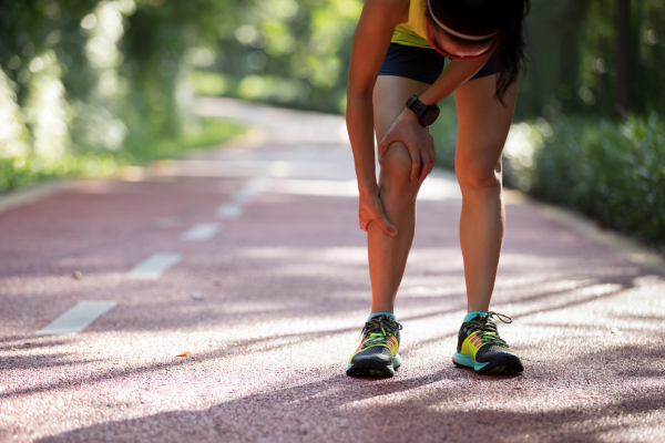 Woman runner holding shin in pain on outdoor track