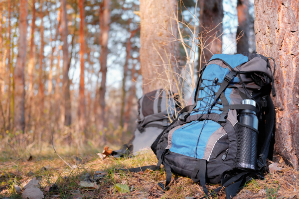 Hiking backpack with water bottle on ground leaning against tree