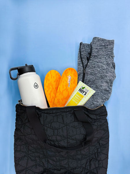 Black bag full of a water bottle, jacket, orange shoe insoles and pain relief cream