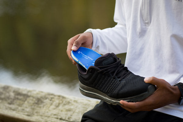 man outside placing blue insole into black shoe