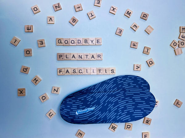 blue shoe insoles next to wood letter blocks spelling “goodbye plantar fasciitis.”