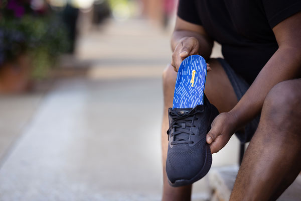 man placing low arch insole into black tennis shoe
