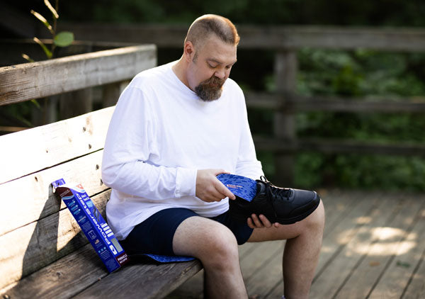 man sitting on park bench placing blue insole into black shoe