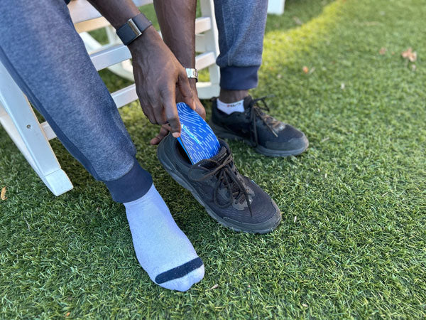 man placing arch support insole into black shoe while on the grass