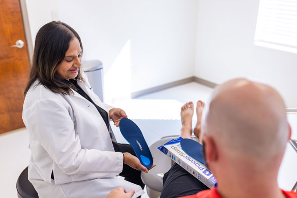 female podiatrist showing male patient a blue orthotic insole