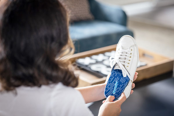 woman placing blue orthotic insole into white shoe