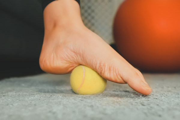 Person rolling tennis ball under foot