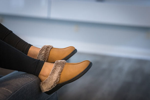 closeup of person draping their legs over a couch arm while wearing brown clog style orthotic slippers