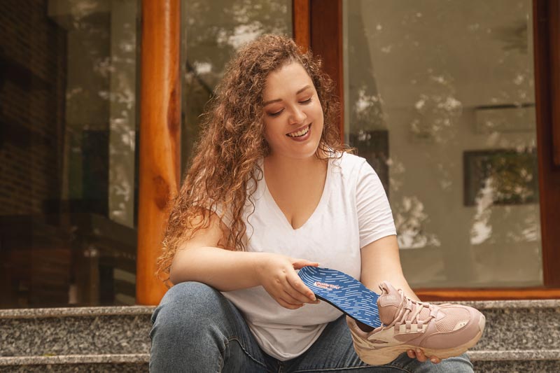 Woman placing flat feet insole into pink shoe