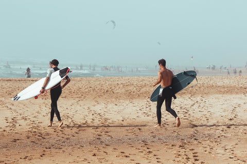 Surfeurs qui courent sur la plage en combinaison néoprène