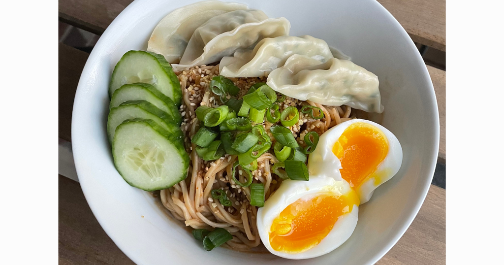 Peanut butter noodles topped with cucumbers, soft boiled eggs and gyozas