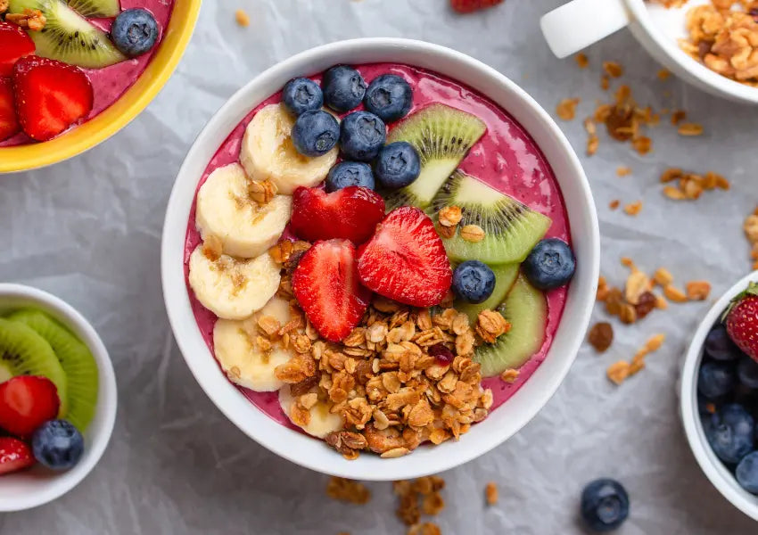 vegan acai bowl with sliced fruits like bananas, strawberries, kiwis, blueberries, and seeds