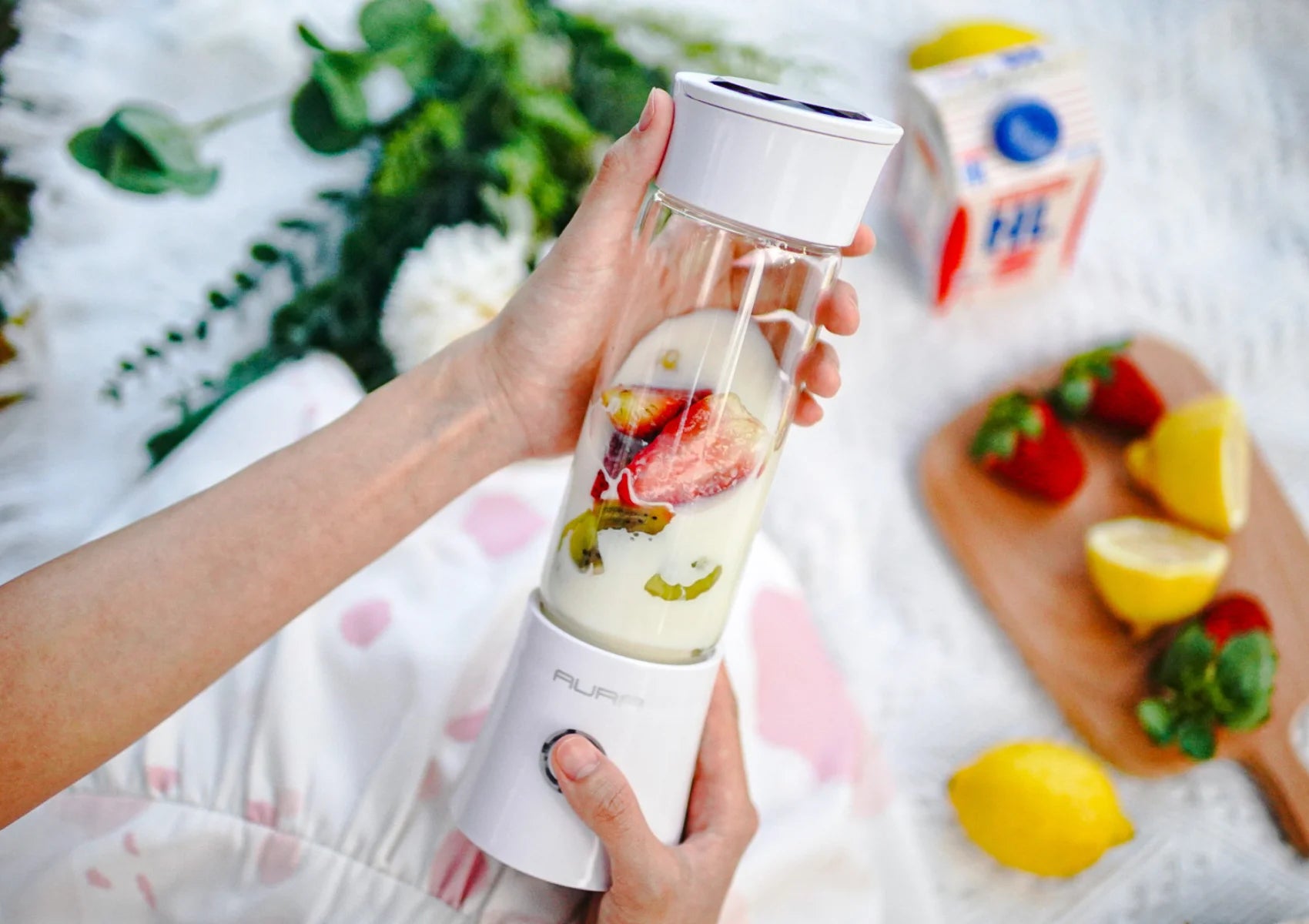 hands holding aura portable blender with fruits and milk inside borosilicate glass jar