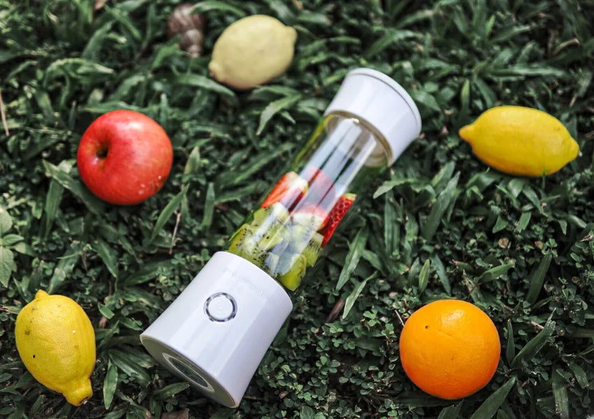 apples, lemons and oranges surrounding the aura portable blender on grass patch