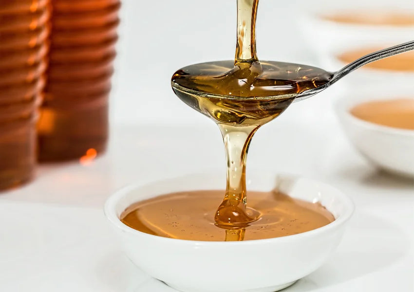 spoonful of natural honey pouring into white bowl