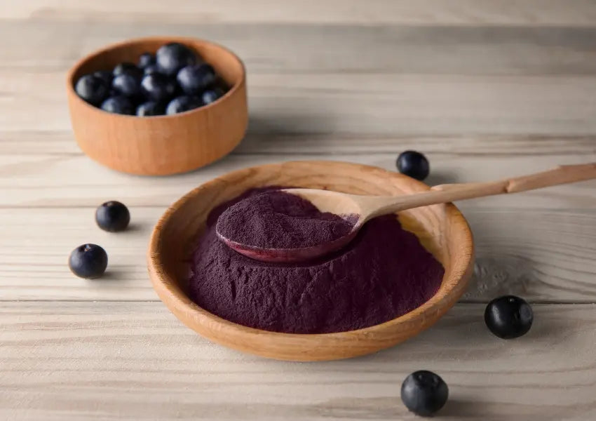 acai powder on a wooden spoon beside a bowl of acai berries