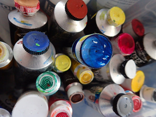 Photo of tubes of paint in a container, with all of their caps painted different colours