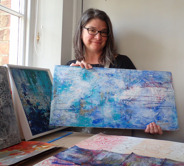 Kimberli Werner posing with abstract mixed media paintings