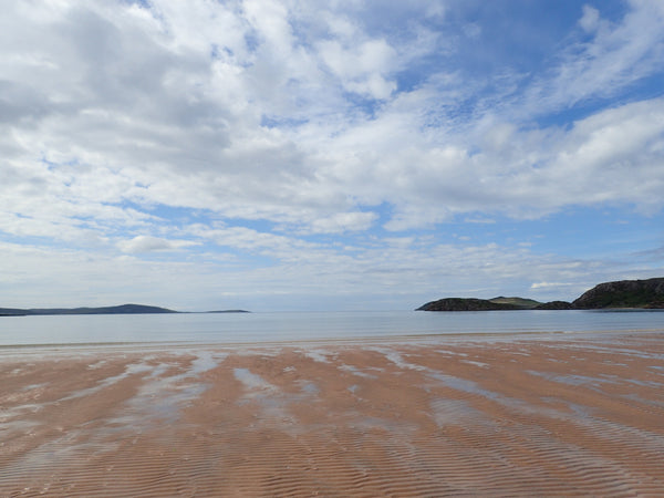 View of Gairloch Beach, Scotland, blue sky with white fluffy clouds, and beach horizon