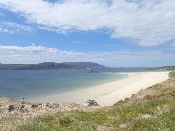View of Durness beach, Scotland, blue sky with white fluffy clouds, beach horizon with a curve of green land going around it.