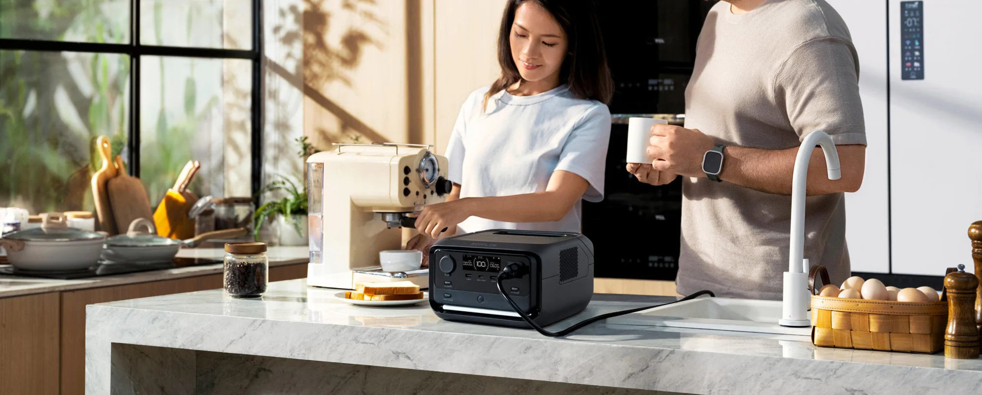 A woman uses a coffee machine on a kitchen counter, while a man stands beside her with a mug. The EcoFlow RIVER 3 Plus 600W 286Wh Portable Solar Power Station by Ecoflow powers the coffee maker as sunlight streams through large windows.