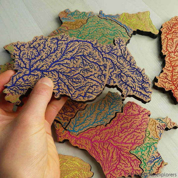 A photo showing a hand picking up a piece of the wooden puzzle made out of Grasshopper Geography's river basin map of France.