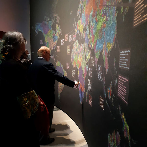 Grasshopper Geography's river basin map of the world on the exhibition Nous, les Fleuves in the Musée des Confluences. Visitors stand in front of the map examining it, pointing to a basin in Africa, telling stories.