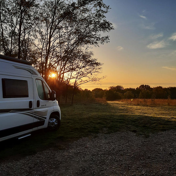 Una autocaravana estacionada en lo alto de una colina, con el amanecer brillando entre los árboles.