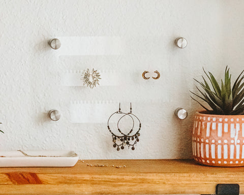 10 x 6 clear acrylic earring holder hanging on the wall with silver hanging hardware and several pairs of earrings hanging on it