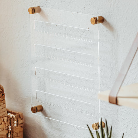 clear acrylic earring holder with gold hardware hanging on the wall